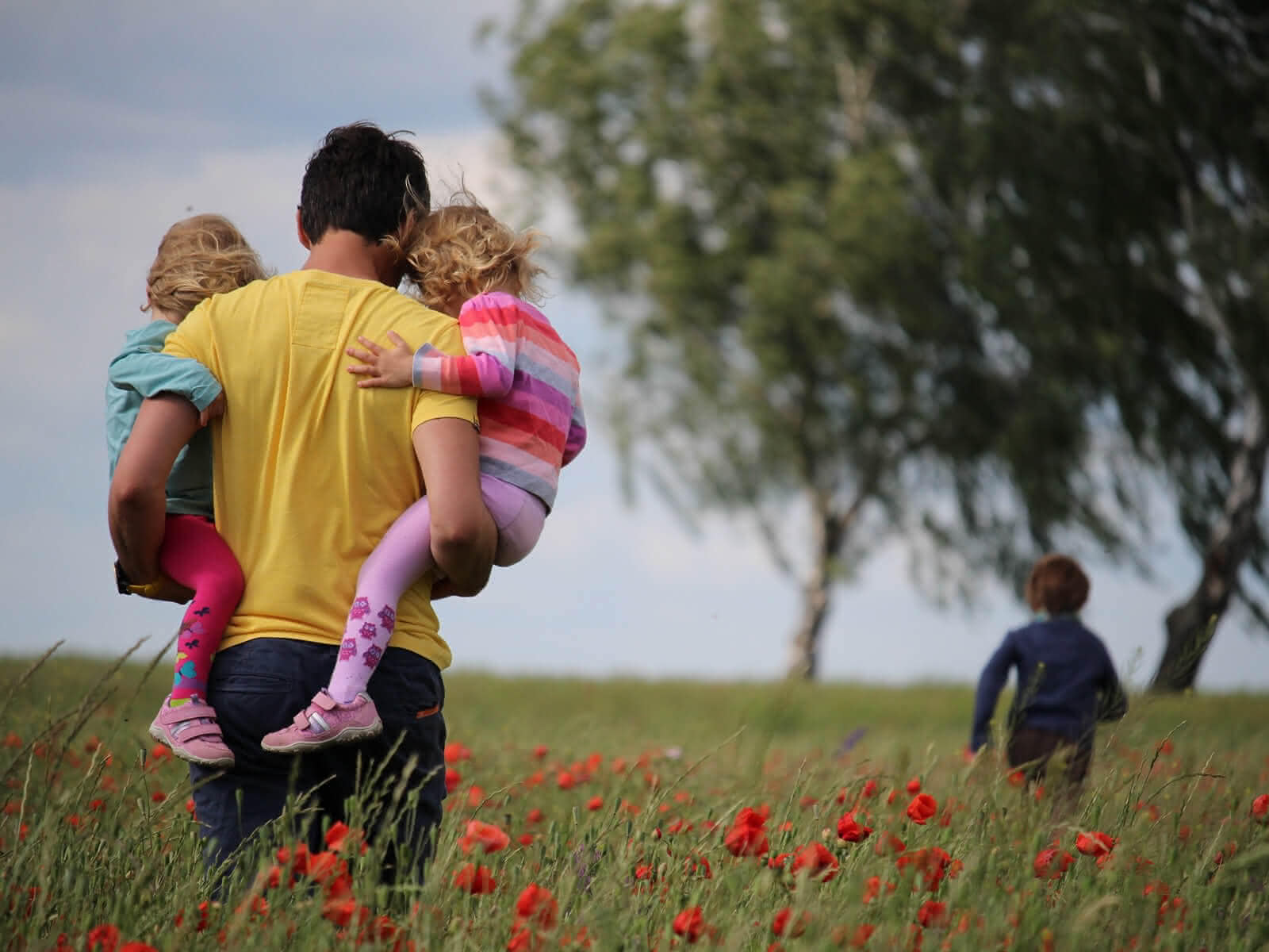 Mann der zwei Kinder in einer Wiese trägt